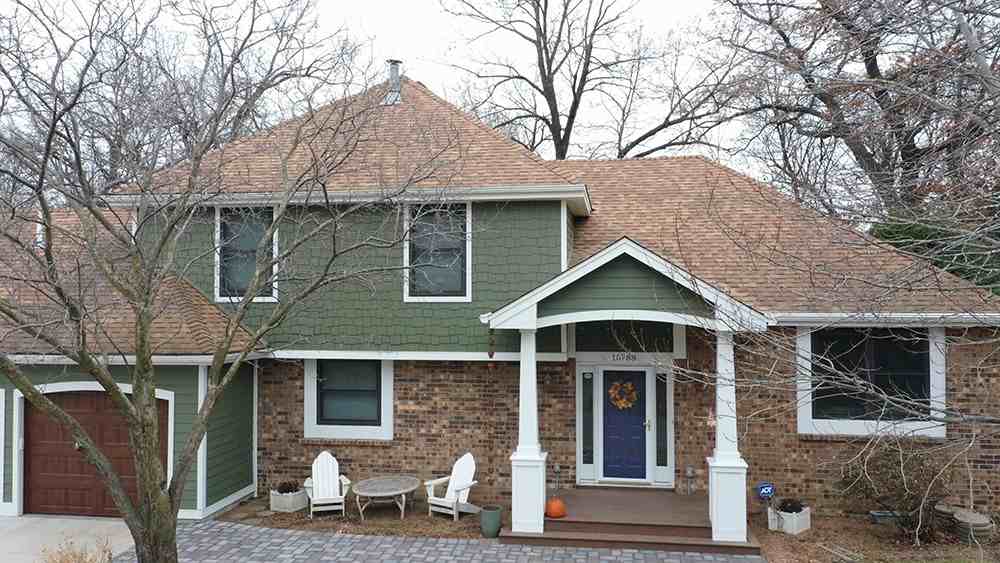 red brick house and sage green colour and white pillars and wooden door and white chairs outside of the door 