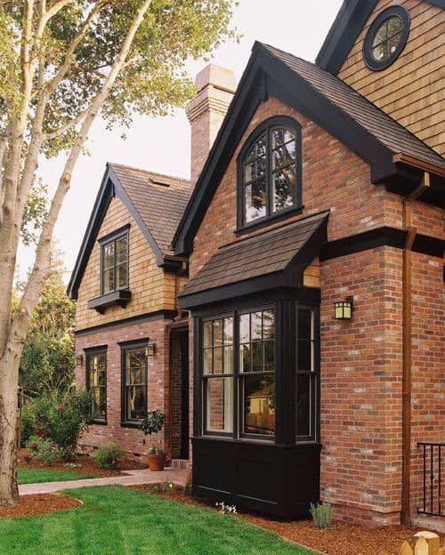 Red brick house charcoal trim and glass window and garden outside of the house