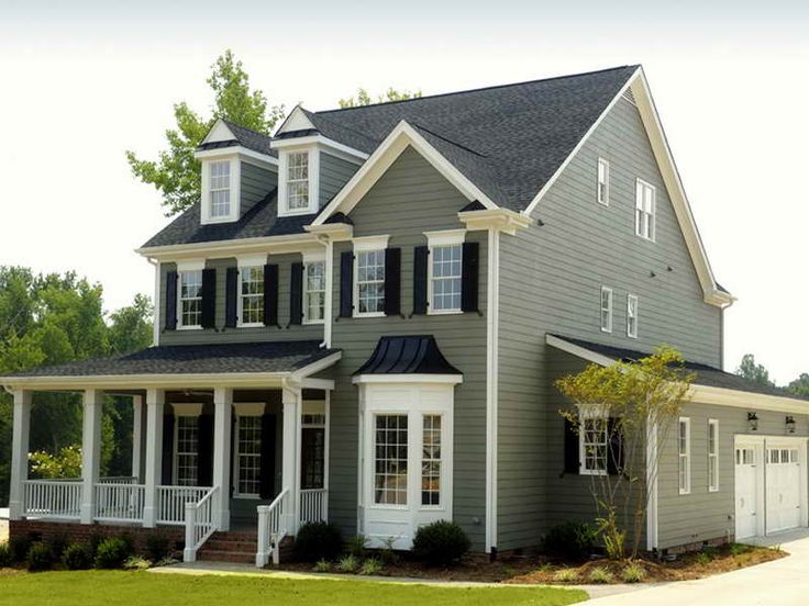 A green house with white windows and shutter and garden outside of the house