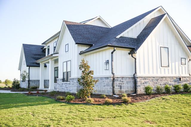 A white house with stone base and black roof and garden outside of the house