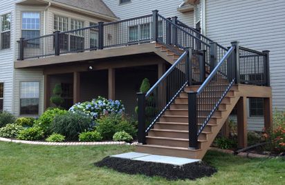 A tan house with windows and railing and stairs and garden outside of the house