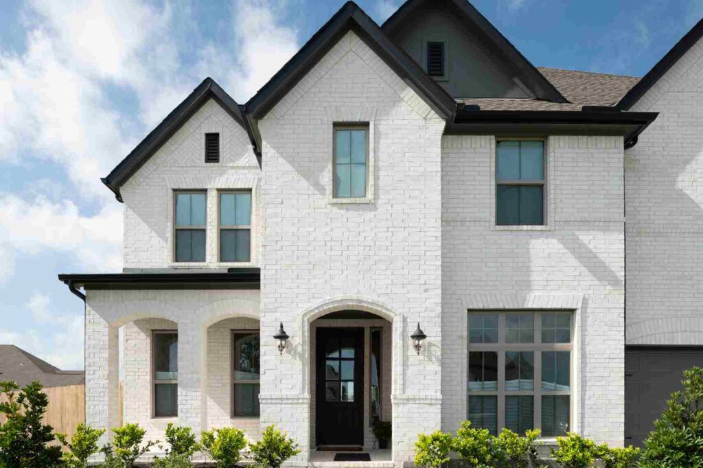 White brick house and windows and black scones on the wall and black glass door 