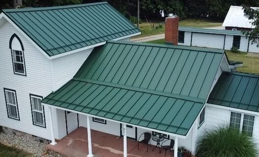 White house with green roof and black trim windows and chairs outside of the house