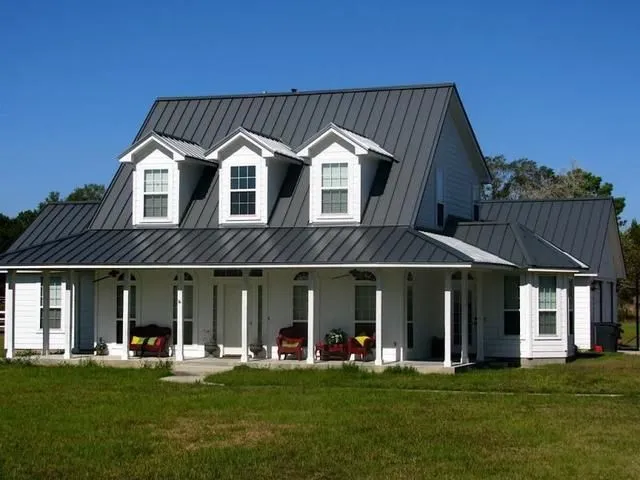 A white house with black metal roof and white pillars 