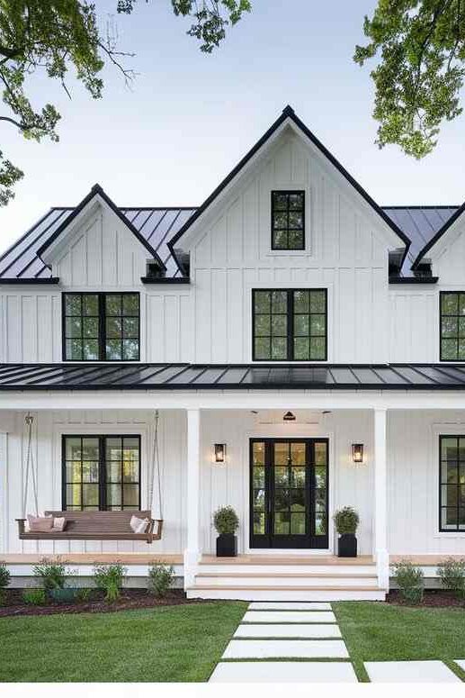 White house with black roof anf glass windows and lights on wall and garden outside 
