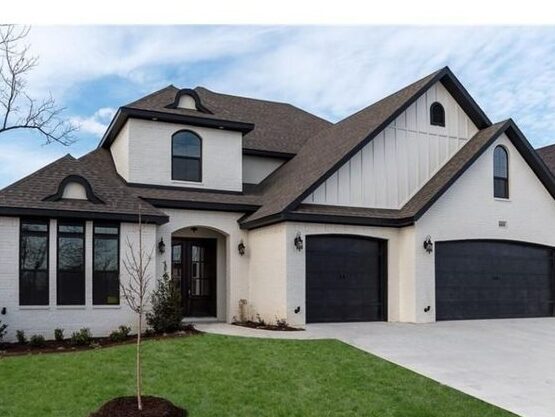 White house with brown trim house and black windows and garden outside of the house