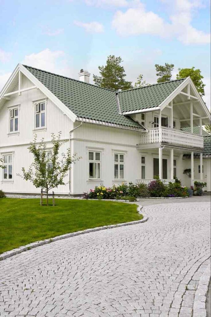 White house with green roof and white windows and garden on the side of the house and pathway outside of the house