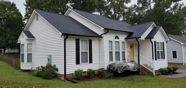A white house with black gutter and white windows and garden outside of the house