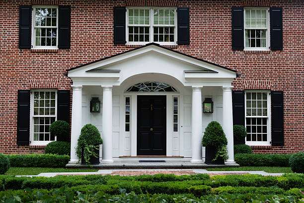 Red brick house with white framed windows and black front door garden outside of the house and mat on the floor