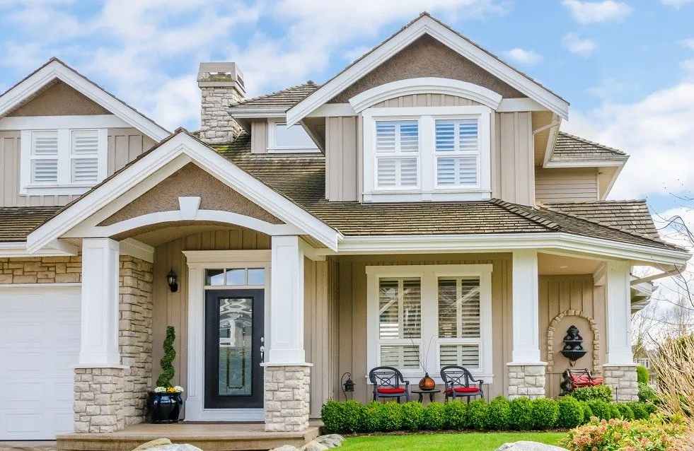 Light tan house with white windows and black door and chairs and table outside of the house