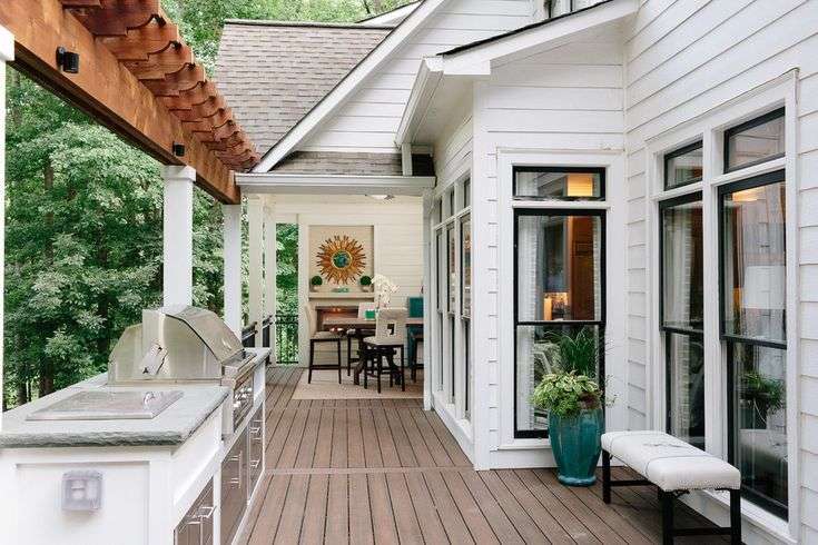 A white house with wooden deck and a table on the deck and black trim windows