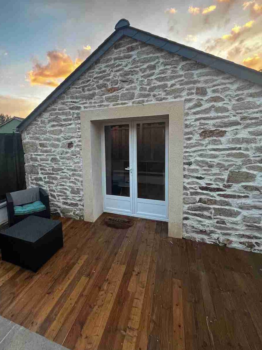 A natural stone house with wooden deck and sofa and chairs outside of the house and mat on the floor