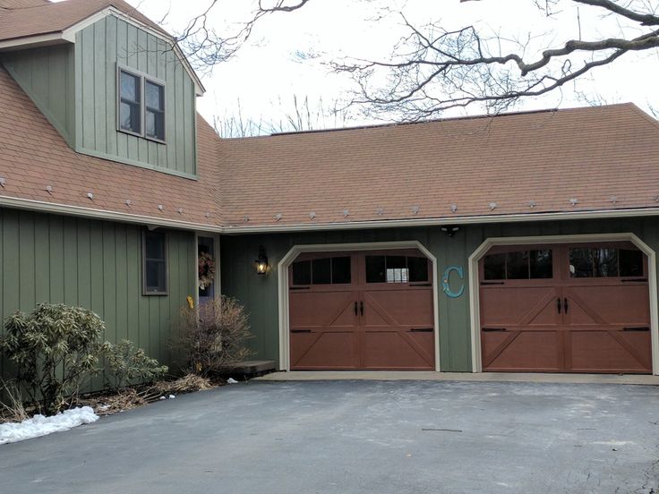 Green house with wooden garage door and lights on the wall