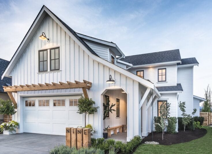 Wooden overhang on white house and lights on the wall and black trim windows