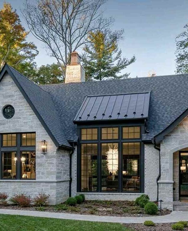 Stone house with black trim windows and lights on the wall and wooden roof 