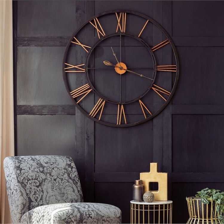 A clock on black wall and grey sofa and small table 
