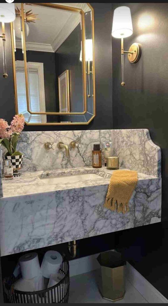 A grey bathroom with black and white marble sink with gold framed mirror on the wall 