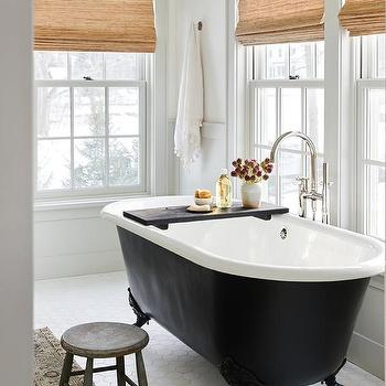 A white bathroom with black bathtub and flower vase on black tray