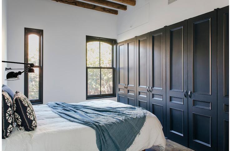 A white bedroom with black closet and black framed windows 