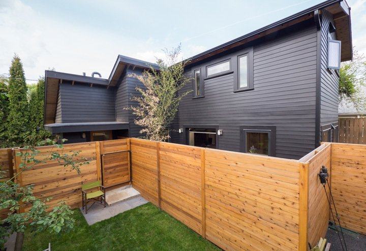 A cedar fencing around on the black house with wooden framed windows