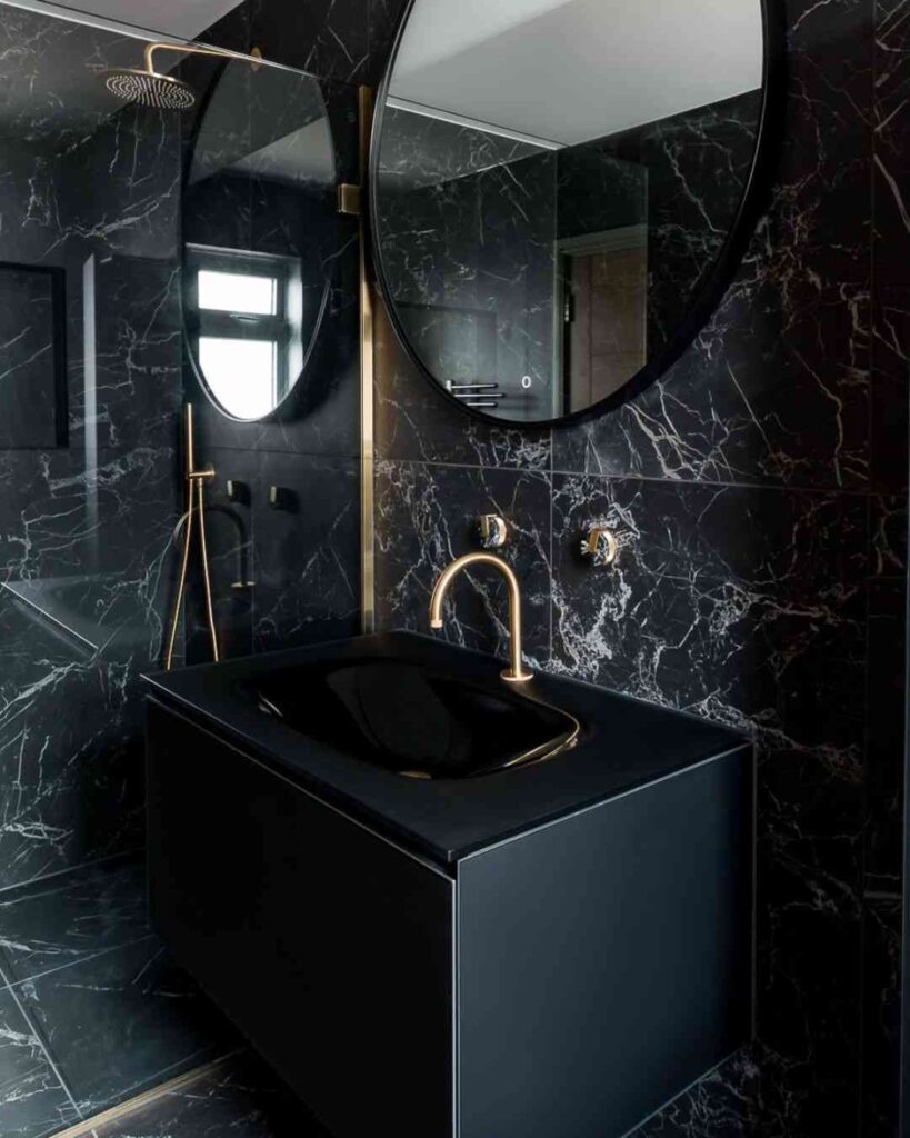 A black marble sink with gold tap and mirror