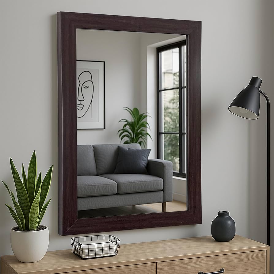 A grey wall with brown framed mirror and a vase on the wooden table