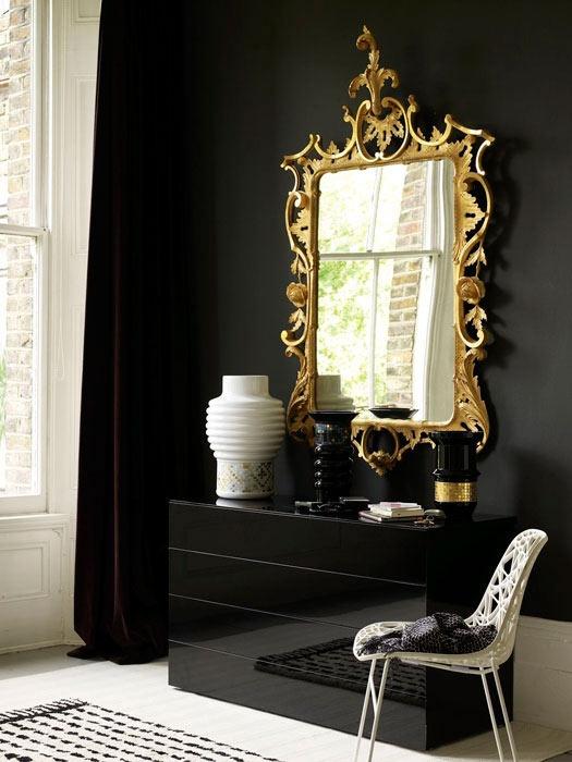 A gold framed mirror on black wall and chair 