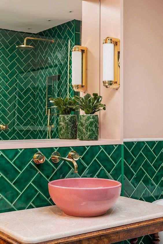 A green bathroom with pink sink and gold fixtures and mirror on the wall 