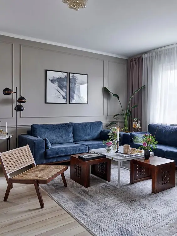 A grey living room with brown and blue sofa and table and a wooden chair and grey rug on the floor