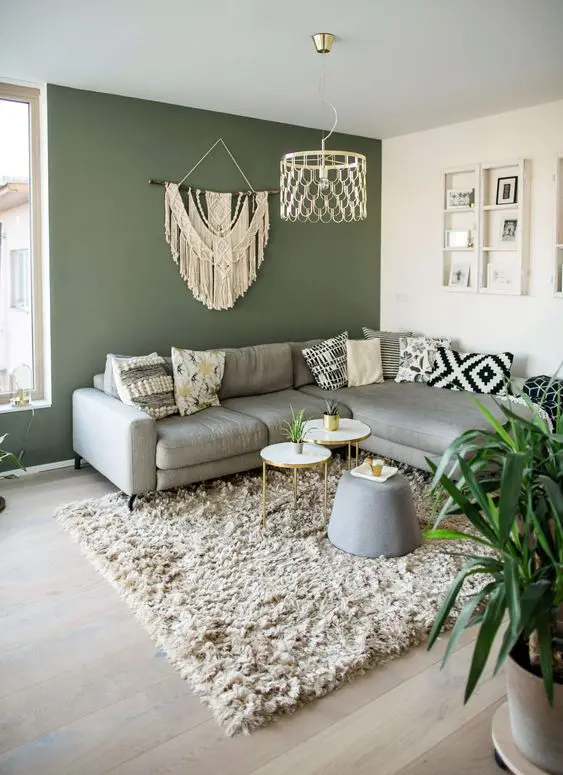 A sage green living room with grey sofa and ottoman and rug on the floor