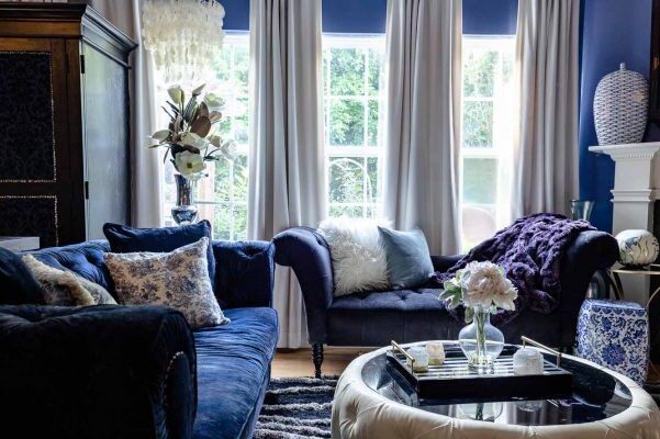 A blue room with white curtains and sofa and cushion on it
