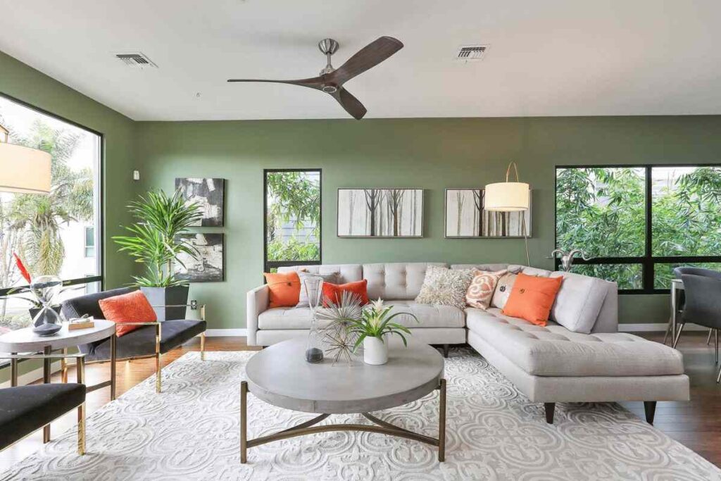 Sage green living room with grey sofa and table and fan above the wall