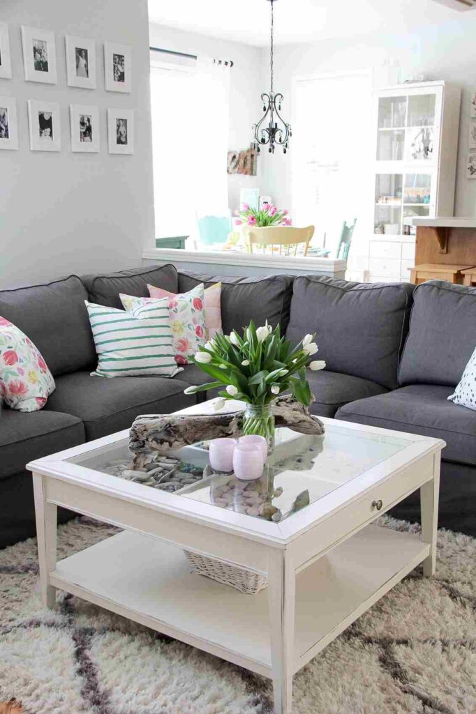 A living room with white coffee table and vase on it grey sofa and cushion on it 