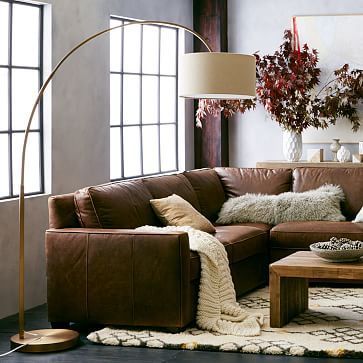 A grey room with white floor lamp and white rug on the floor and brown sofa with cushion