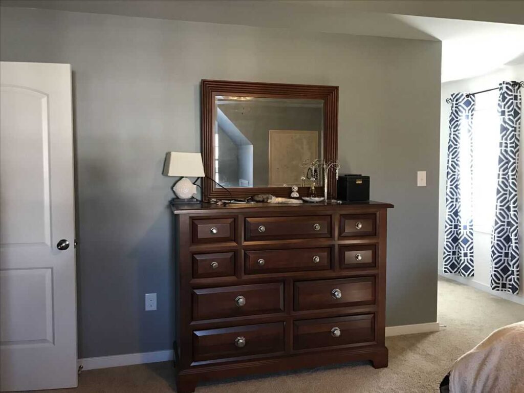 A wooden cabinets with mirror and lamp on it and grey wall and wooden floor