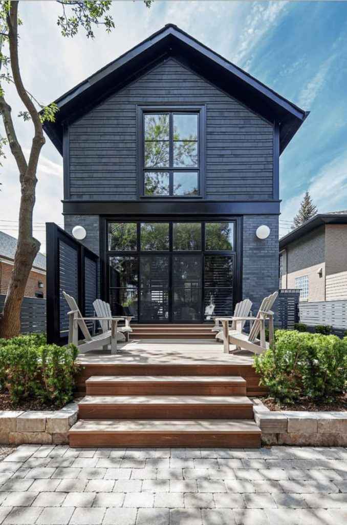 A black house with wooden porch and chairs outside of the house