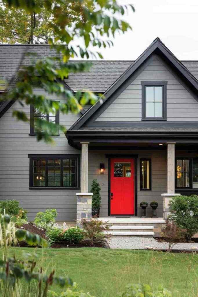 A grey house with black roof and red front door and lights on the wall