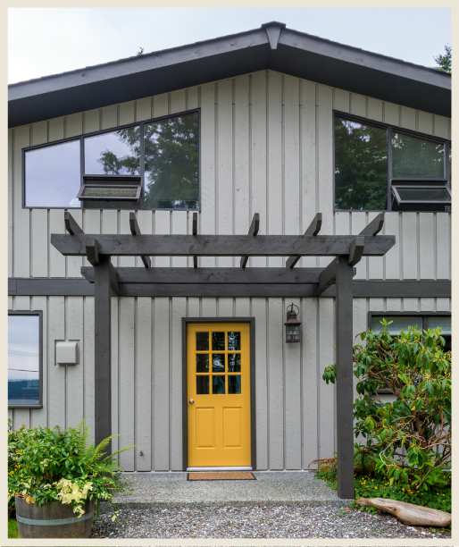 A grey house with yellow door and light on the wall and glass windows