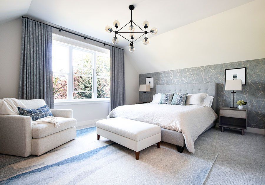 A white a grey bedroom with chair and frames on the wall and white windows 