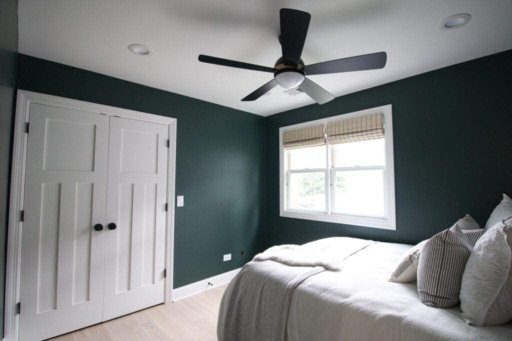 A green bedroom with black celling fan and white trim and windows 