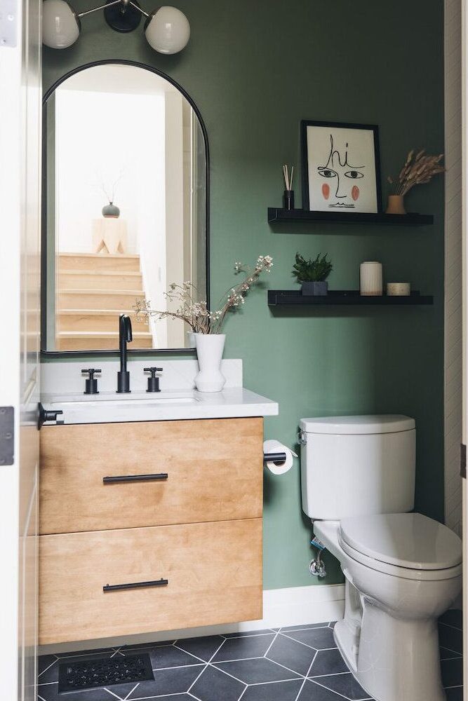 A green bathroom with black shelves and wooden vanity with mirror on the wall 