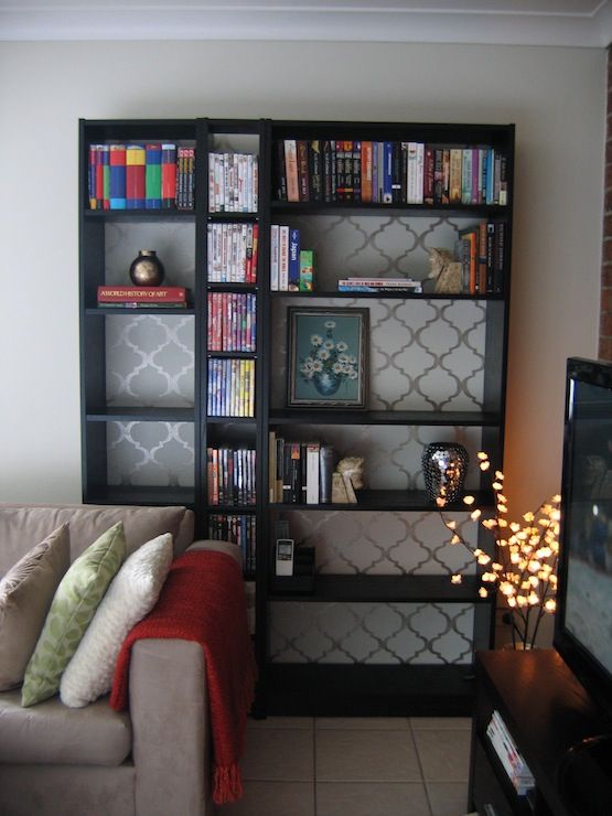 A grey living room with black shelves and sofa with red throw and cushion 