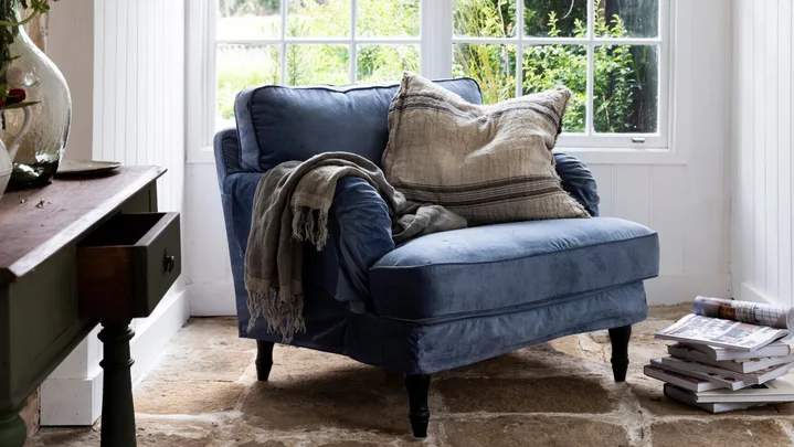 A grey chair with grey pillow and throw and windows  