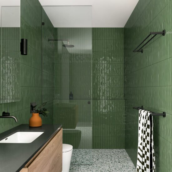 A green bathroom tiles with black shower kit and glass shower door 