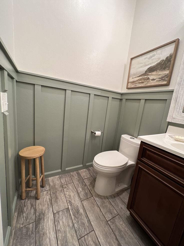 A sage green bathroom with board and batten wall and white accents and frame on the wall 