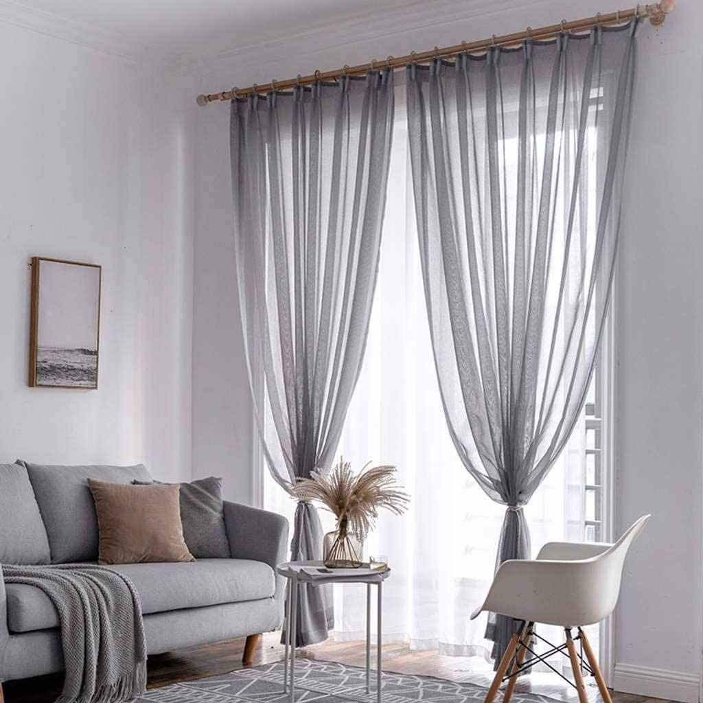 A grey living room with sheer curtain with windows and sofa with cushion and throw 
