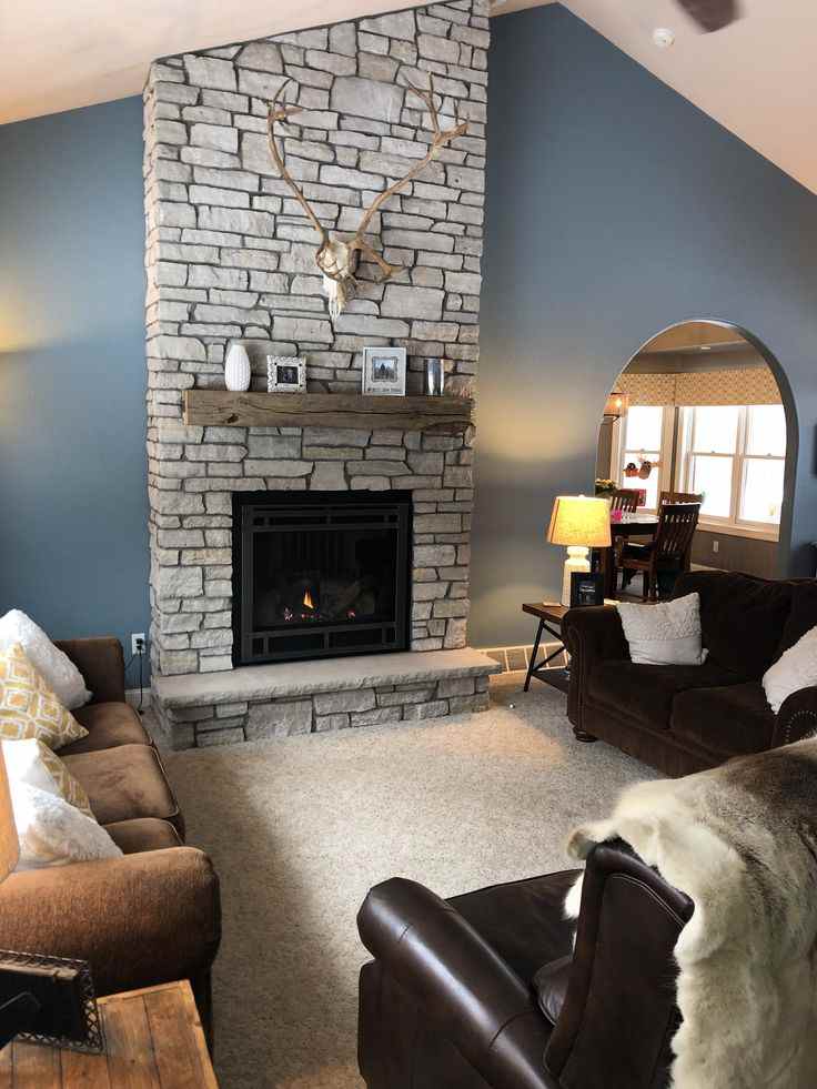 A blue and grey living room with grey stone fireplace and wooden floor and sofa with cushion 