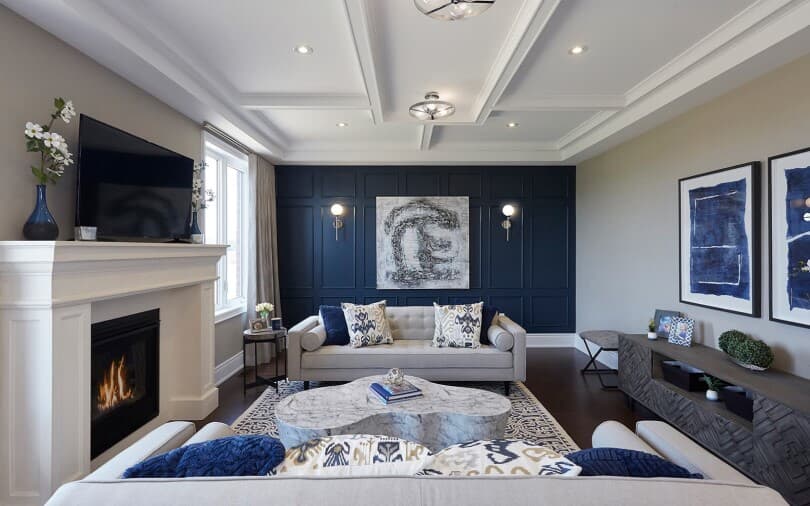 A grey and navy blue wall and grey sofa with cushion and painting on the wall 