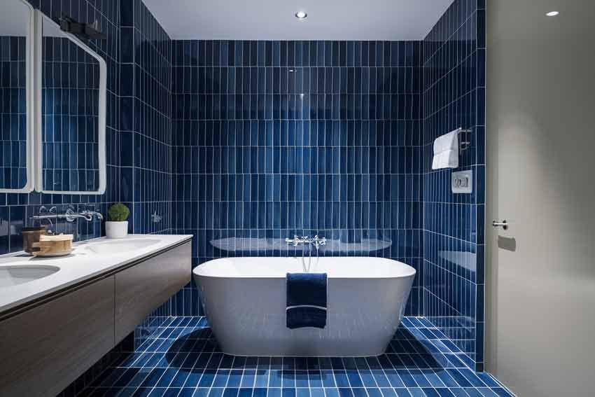 A blue tiles with grey accent and white bathtub and vanity with sink 