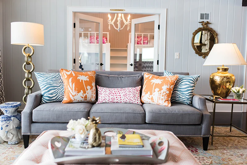 A living room with mirror on the mirror and grey sofa with cushion and lamp on the table 
